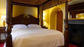 A four-poster bed with a wooden headboard, a red patterned carpet, and a fireplace with a mirror above it.