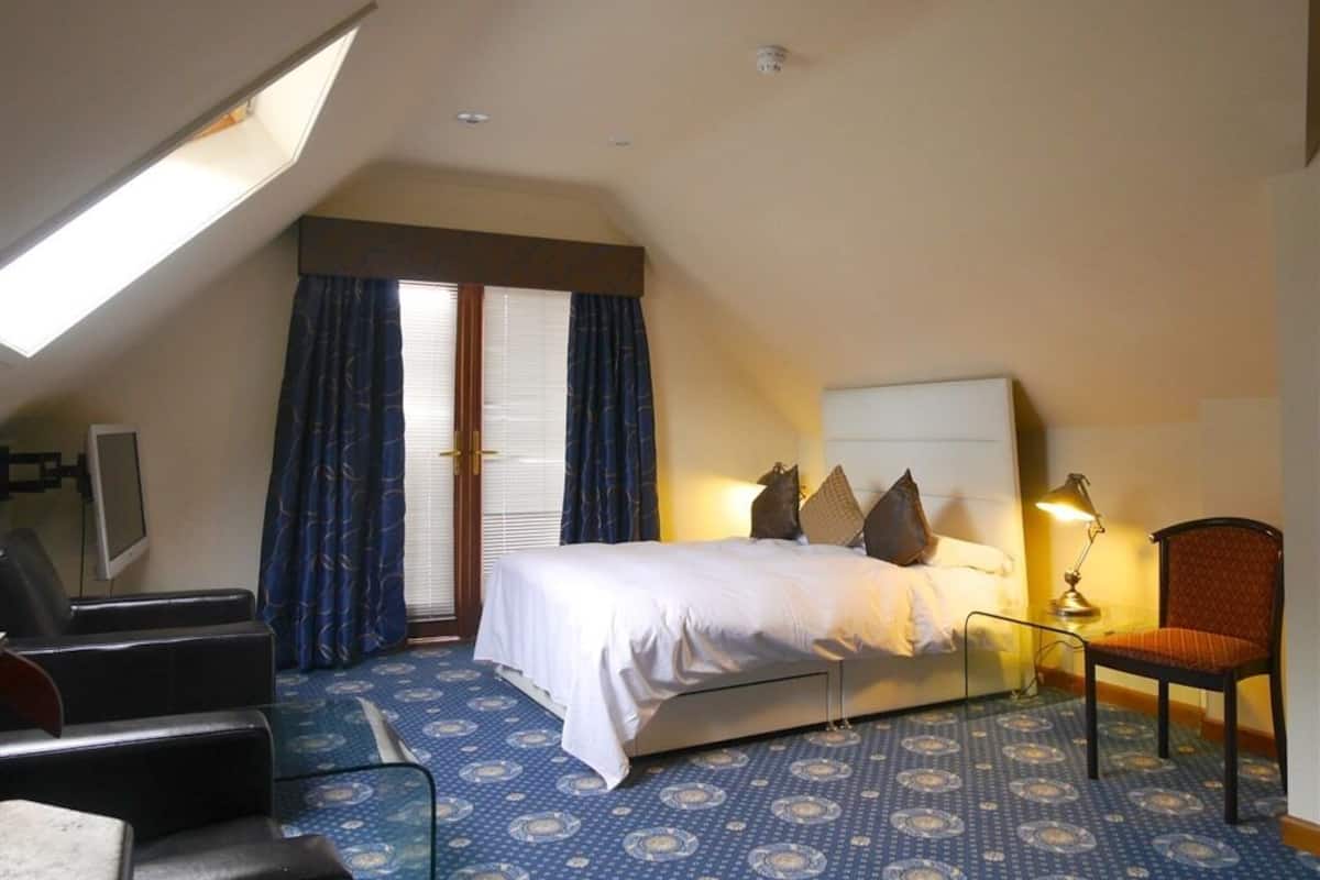 A hotel room with a bed, a desk, a chair, and a window with curtains.