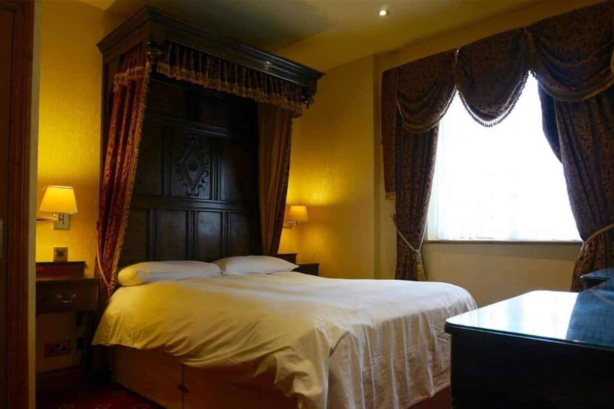 A hotel room with a large bed, two bedside lamps, a wooden headboard, and a window with curtains.
