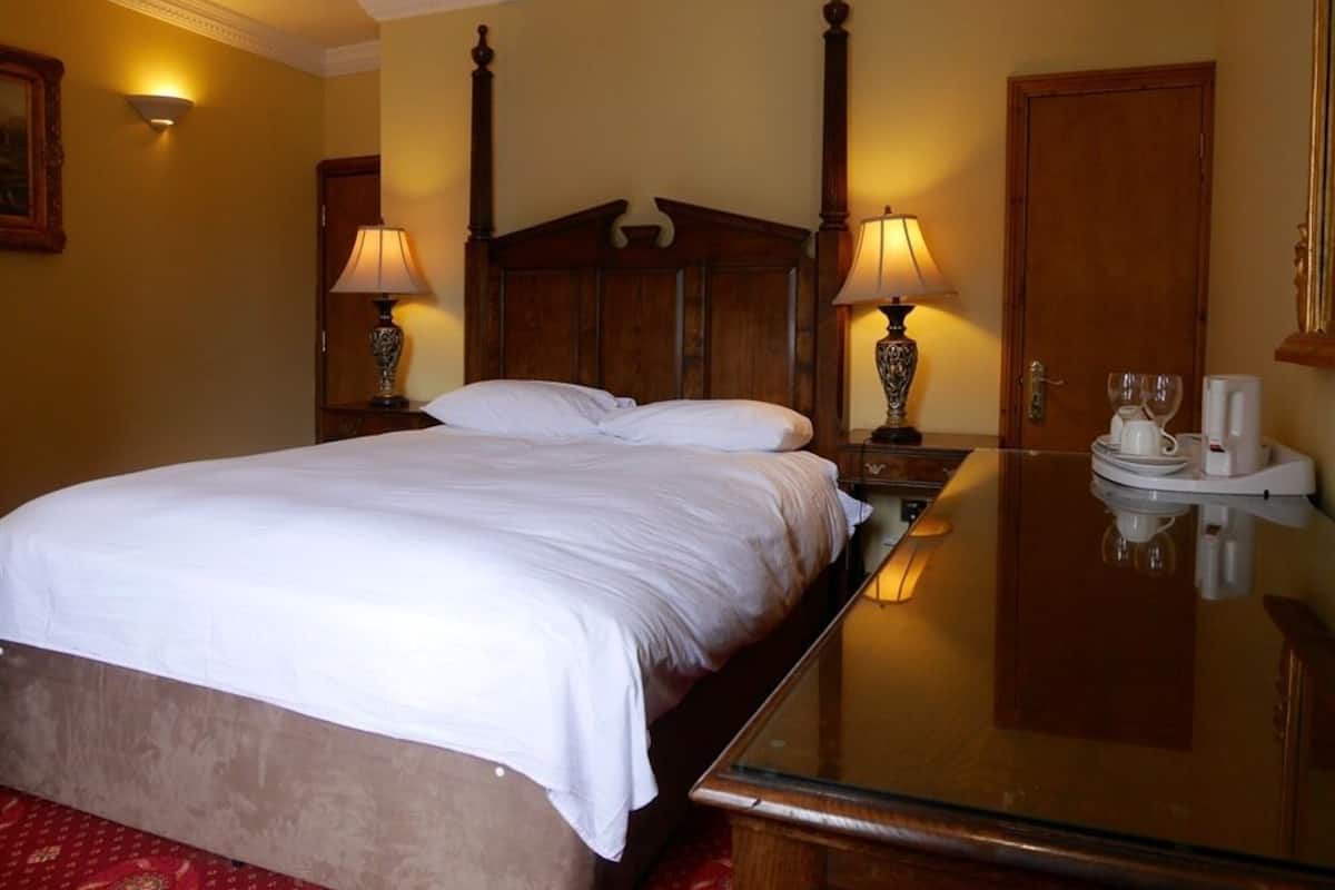 A hotel room with a large bed, two bedside lamps, a bedside table with a glass, and a wooden headboard.