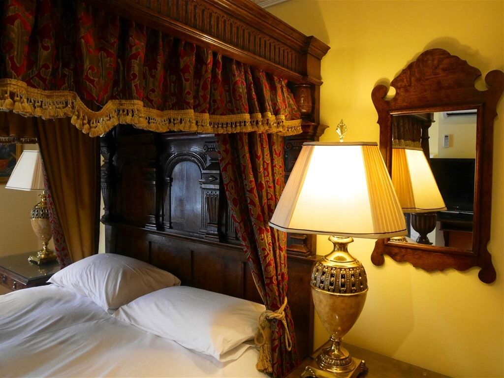 Une chambre d’hôtel avec une tête de lit en bois, un lit recouvert de draps blancs, une lampe décorative et un miroir au mur.