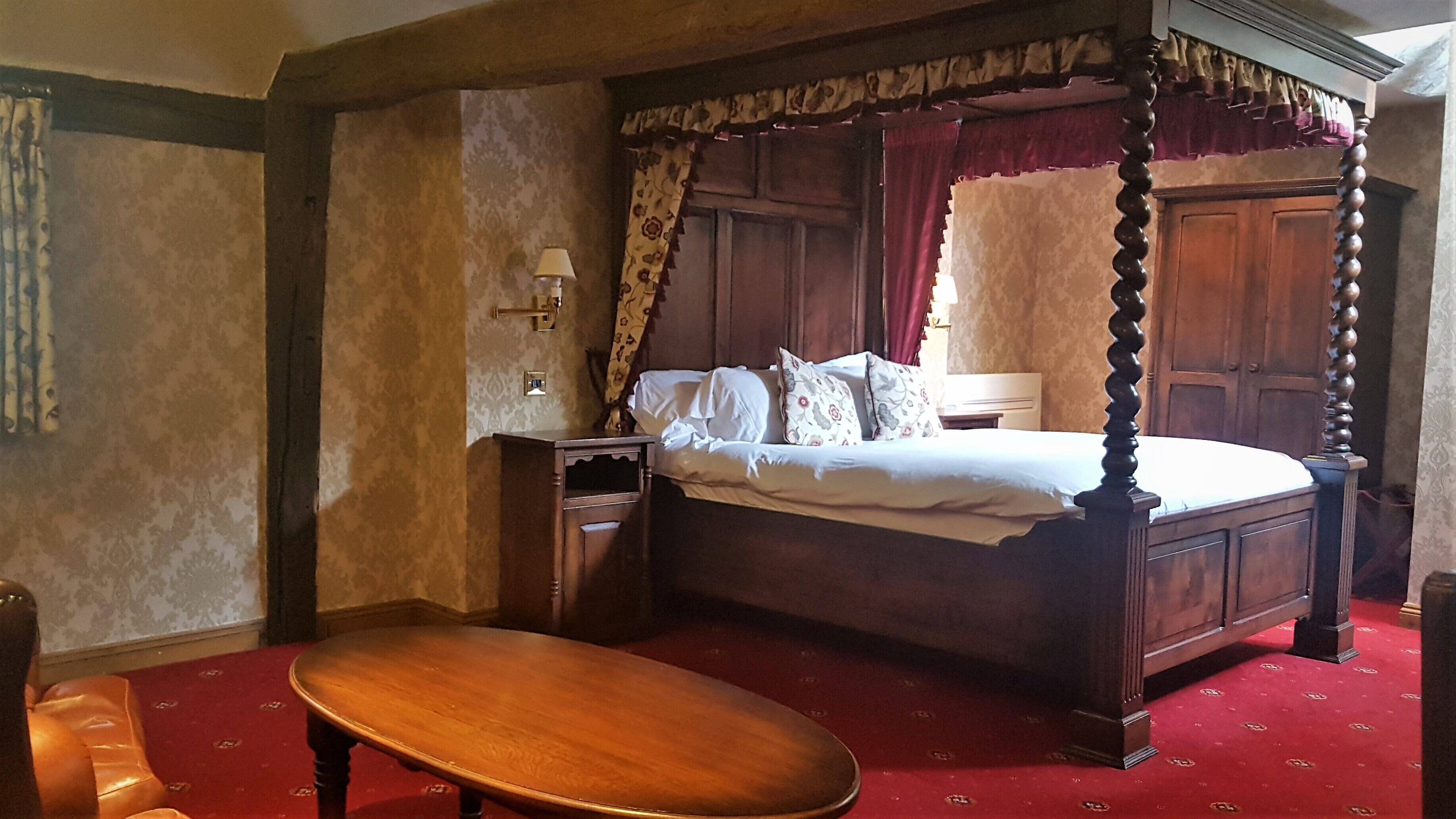 A four-poster canopy bed with a wooden frame, a bedside table, and a red carpeted floor.
