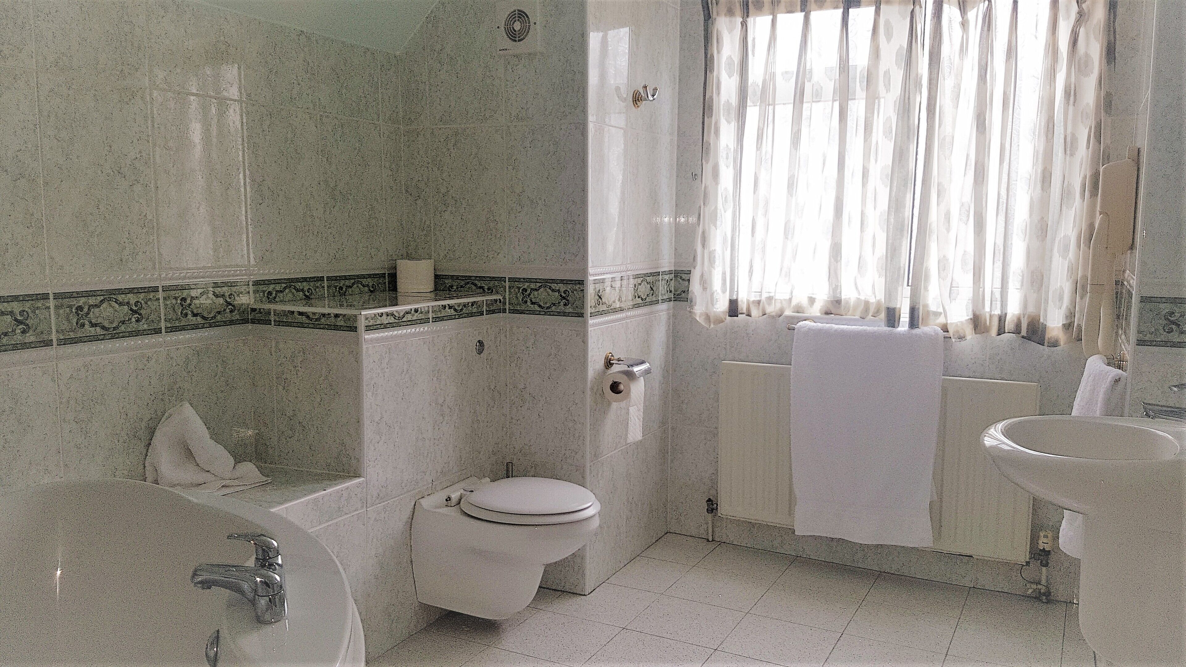 A bathroom with a bathtub, toilet, sink, and a window with curtains.