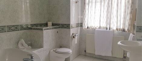 A bathroom with a bathtub, toilet, sink, and a window with curtains.
