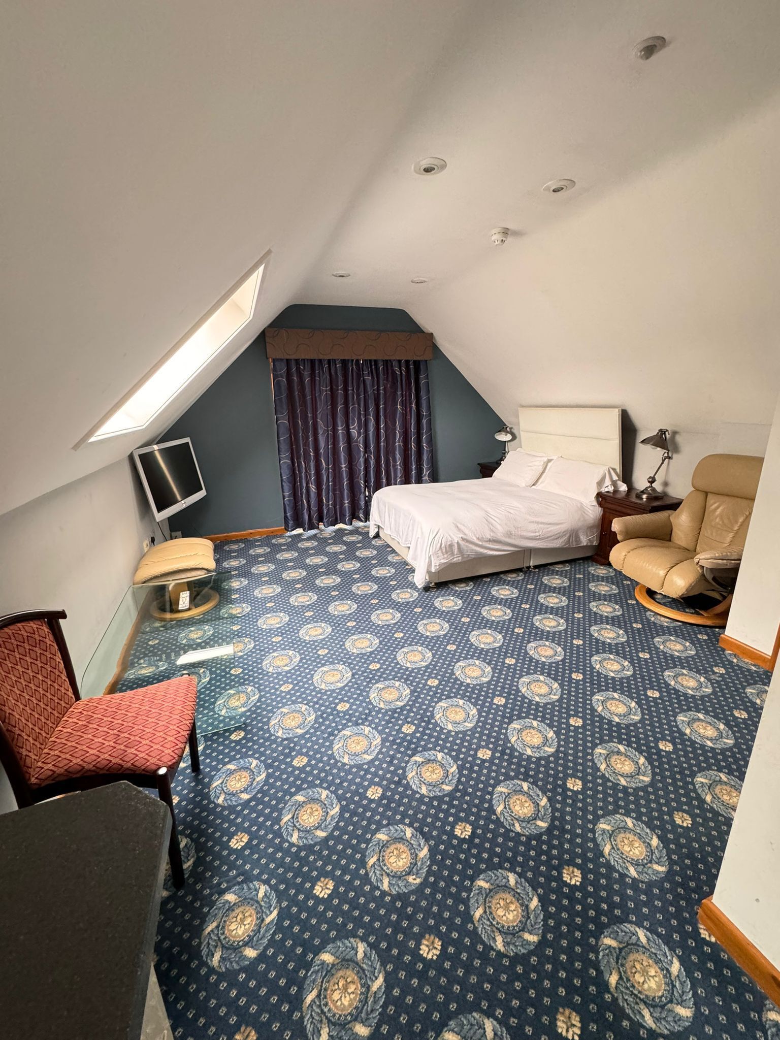 A hotel room with a bed, a desk, a chair, a TV, and a window with curtains.