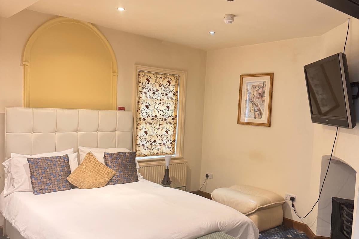 A neatly arranged bedroom with a large bed, a bench, a television, and a window with floral curtains.