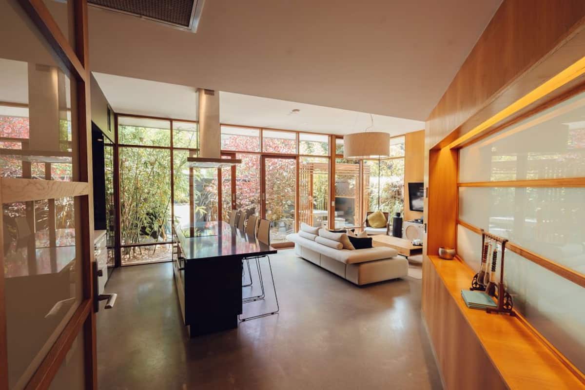 A modern kitchen with a dining table and chairs, a sofa, and a large window with a view of trees.