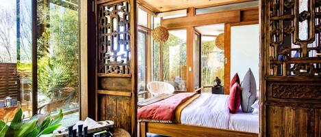 Ein geräumiges Schlafzimmer mit einem großen Bett, Holzmöbeln und Blick ins Grüne durch große Fenster.