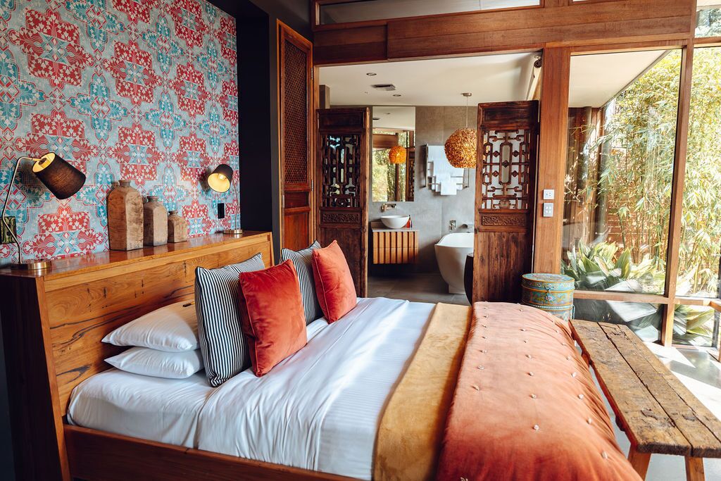 Een slaapkamer met een groot bed, een houten hoofdbord en uitzicht op een badkamer en buitenruimte.