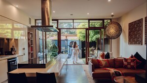 A modern kitchen with a dining area, a large window, and a living room with a sofa and decorative pillows. - Sticky Rice Villas (Stirling)