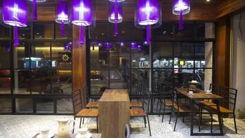 A restaurant with wooden tables and chairs, purple hanging lights, and large windows.
