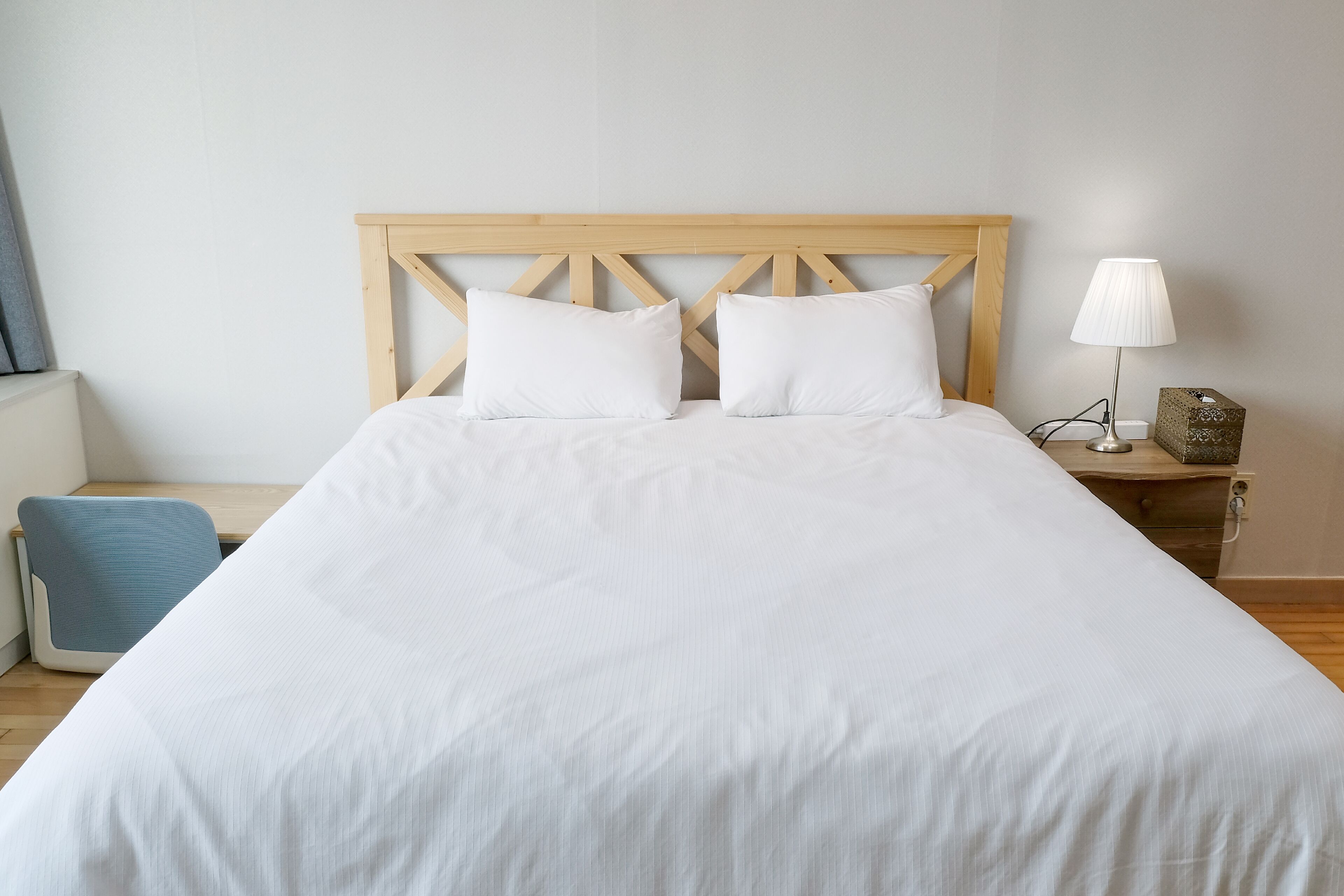 A neatly made bed with a wooden headboard, a bedside lamp, and a tissue box on a nightstand.