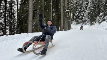 Una persona deslizándose en un trineo por una pendiente nevada en un área boscosa.
