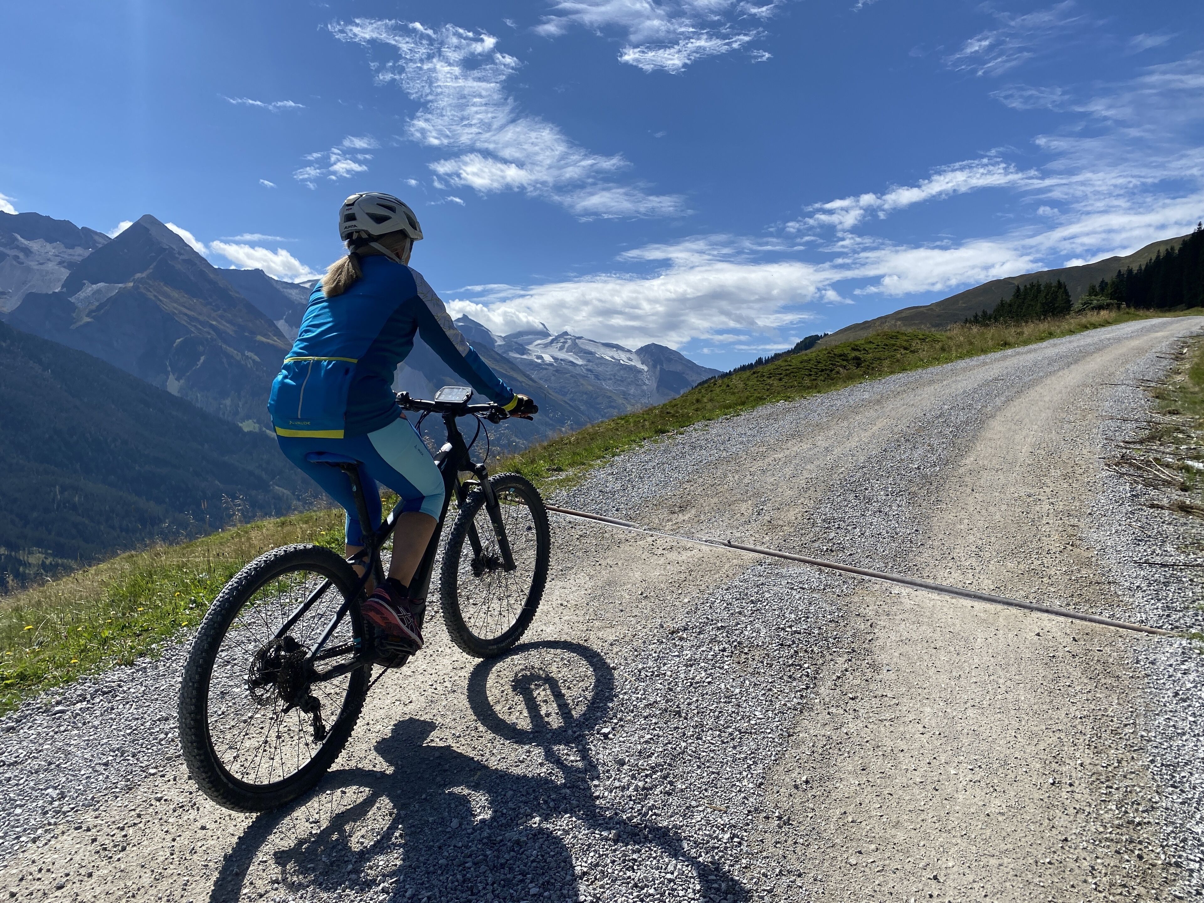 Una persona montando una bicicleta de montaña sobre un camino de grava, con un paisaje montañoso al fondo.
