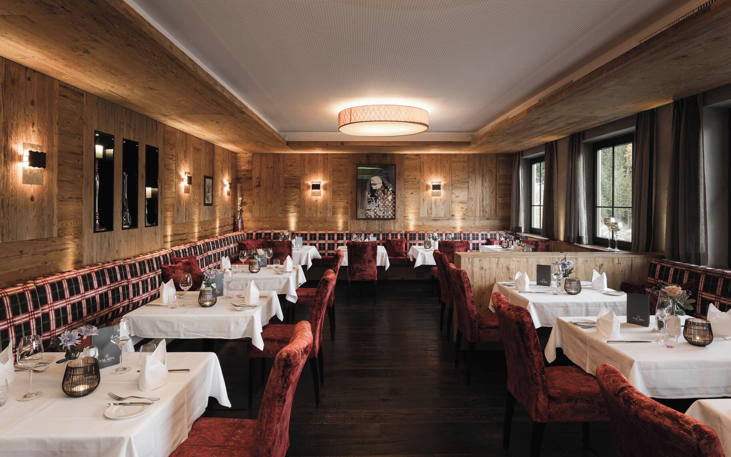 Un restaurante con paredes de madera, mesas blancas y sillas de terciopelo rojo.