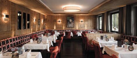 Un restaurante con paredes de madera, mesas blancas y sillas de terciopelo rojo.