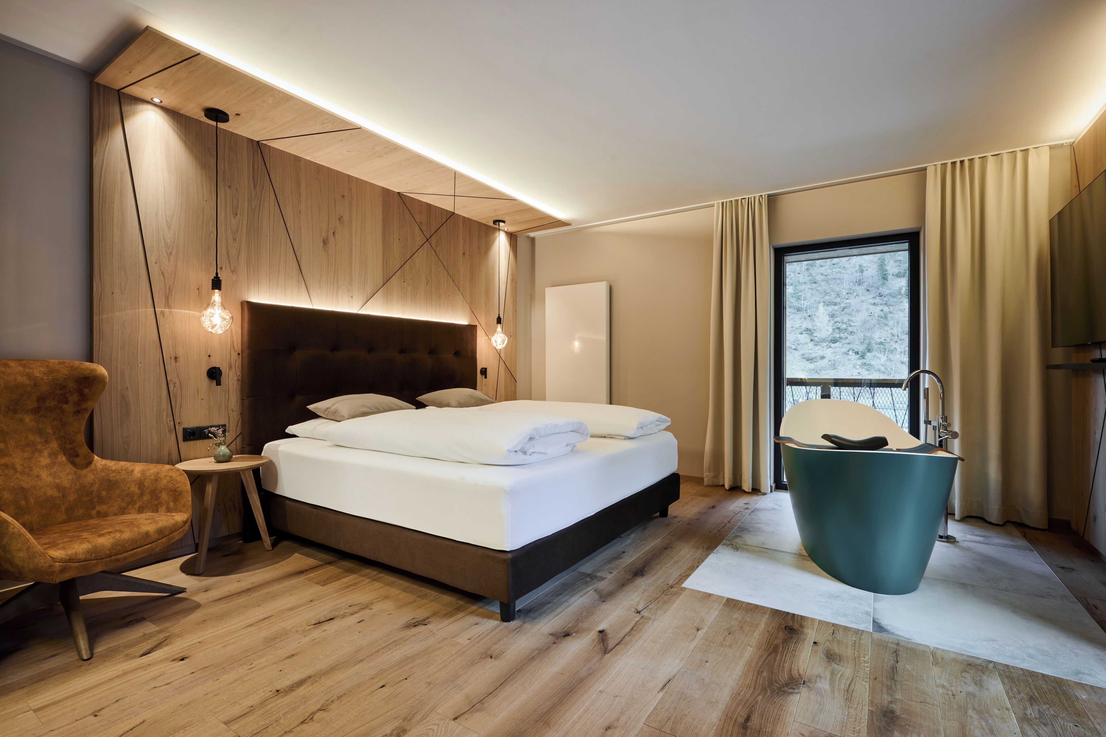 Un dormitorio moderno con cabecera de madera, una cama grande, una silla de madera, una mesa redonda, una bañera y una ventana con cortinas.