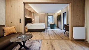 A modern hotel room with a wooden floor, a bed, a sofa, a table, and a TV. -  VALARA Alpine Art Hotel (Tux)