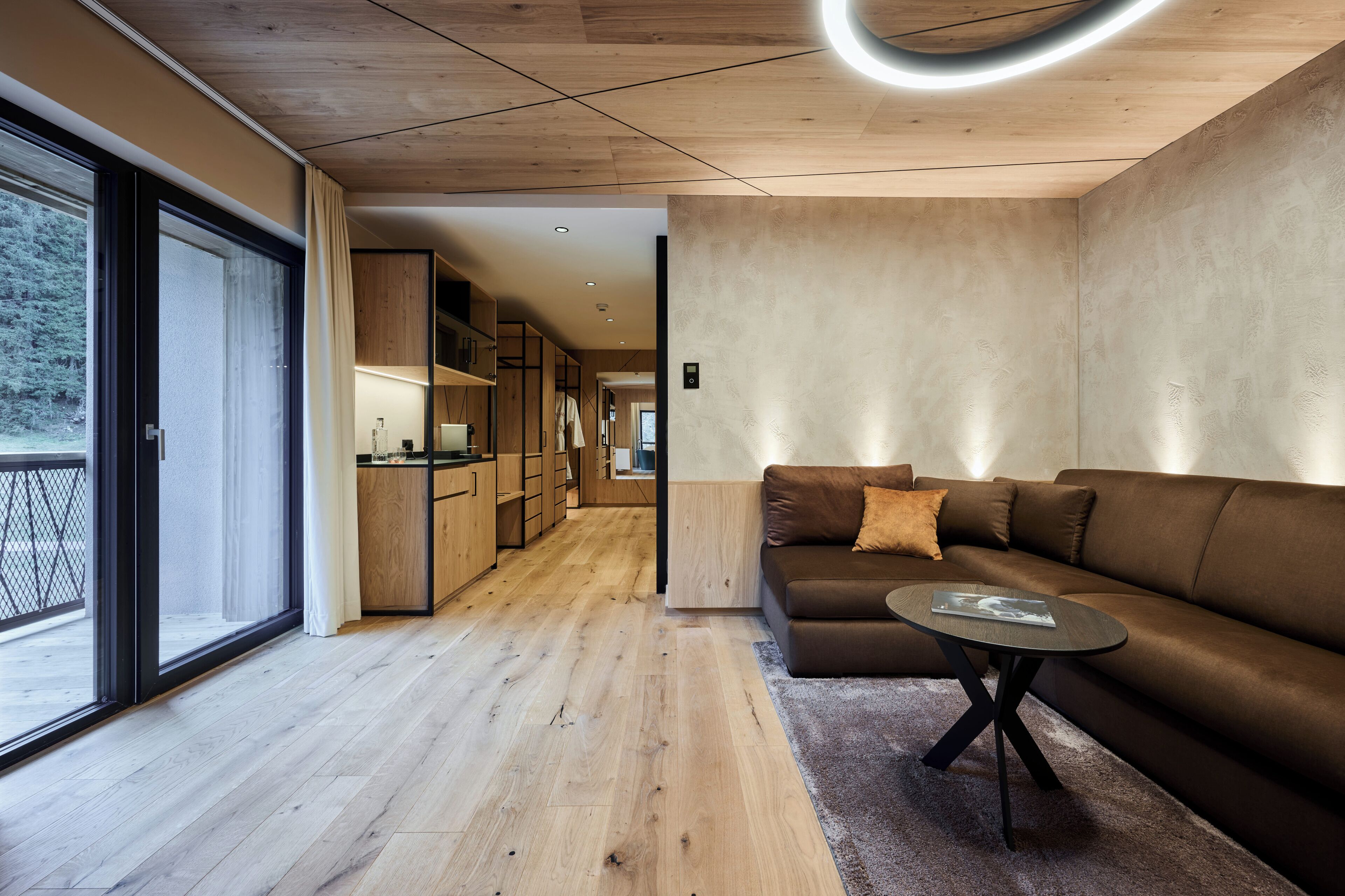 Una sala de estar moderna con un sofá marrón, una mesita de centro y vistas a una terraza de madera a través de amplios puertas correderas.