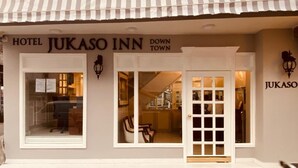 Das Hotel Jukasho Inn mit gestreifter Markise, Glastür und einem einsehbaren Innenbereich mit Sitzgelegenheiten und einer Küchenzeile.