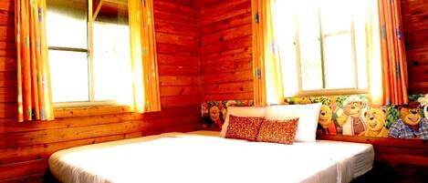 Una habitación de cabaña de madera con una cama grande, dos ventanas con cortinas y un mural temático de osos.