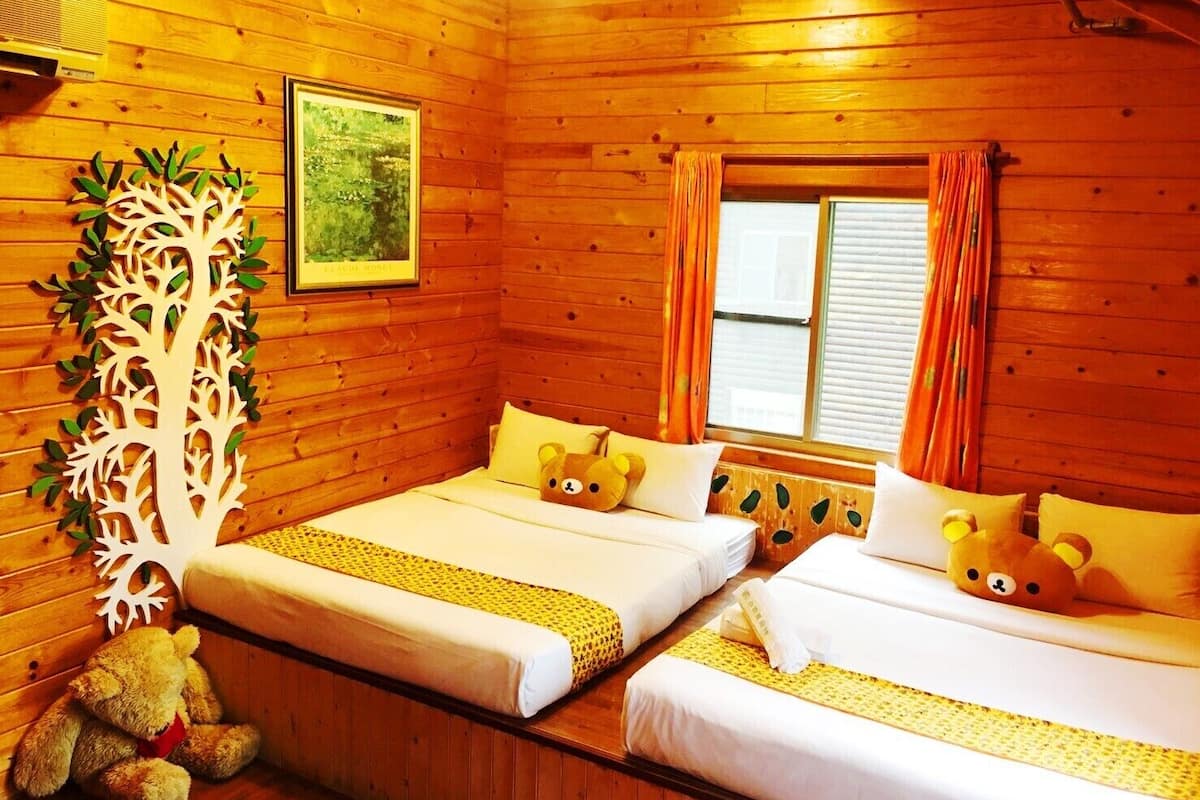 A cozy wooden cabin room with two beds, a teddy bear, a tree decoration, and a framed picture on the wall.