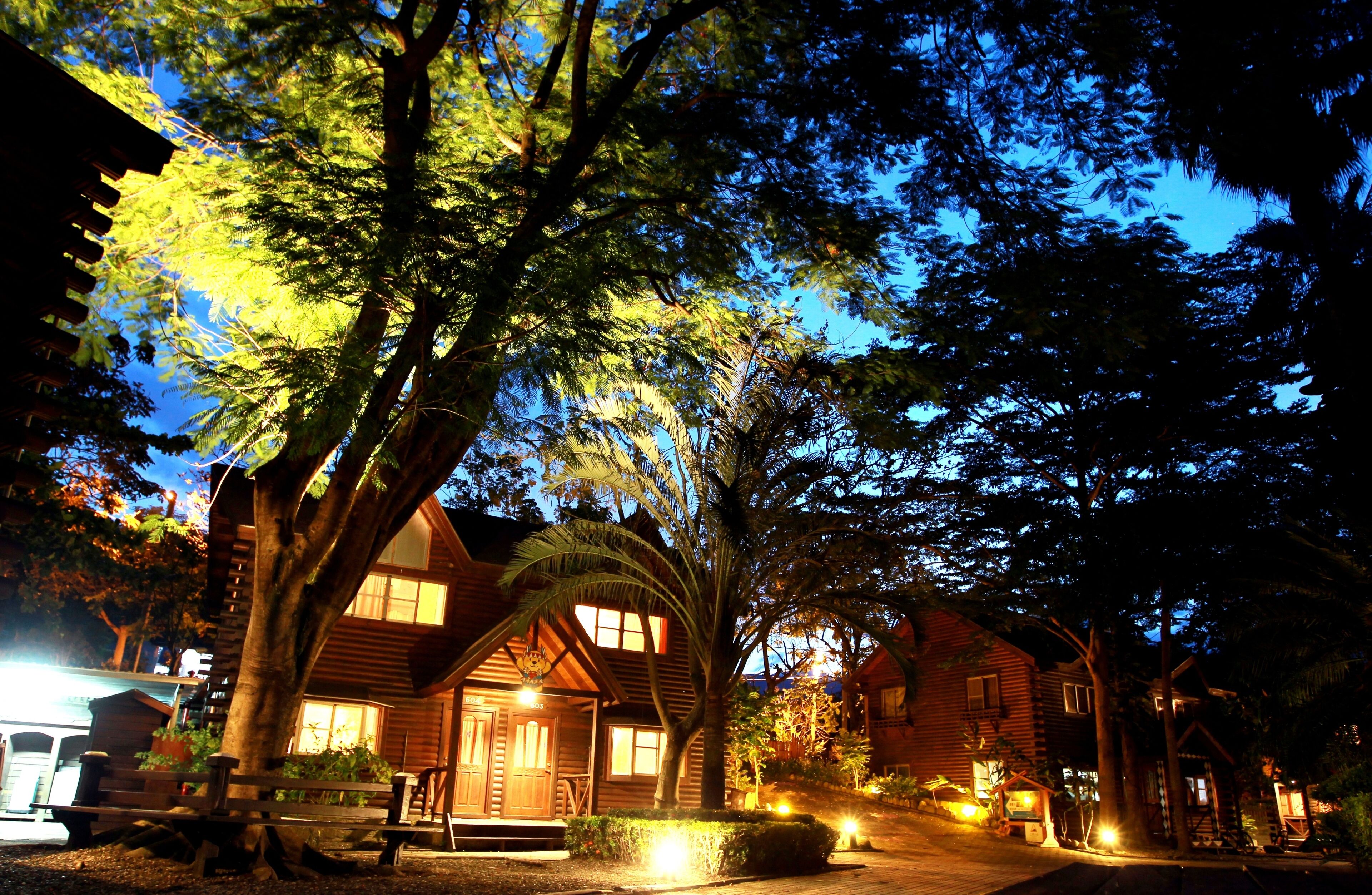 A rustic cabin-style hotel with a prominent wooden structure, surrounded by large trees and a well-lit driveway.