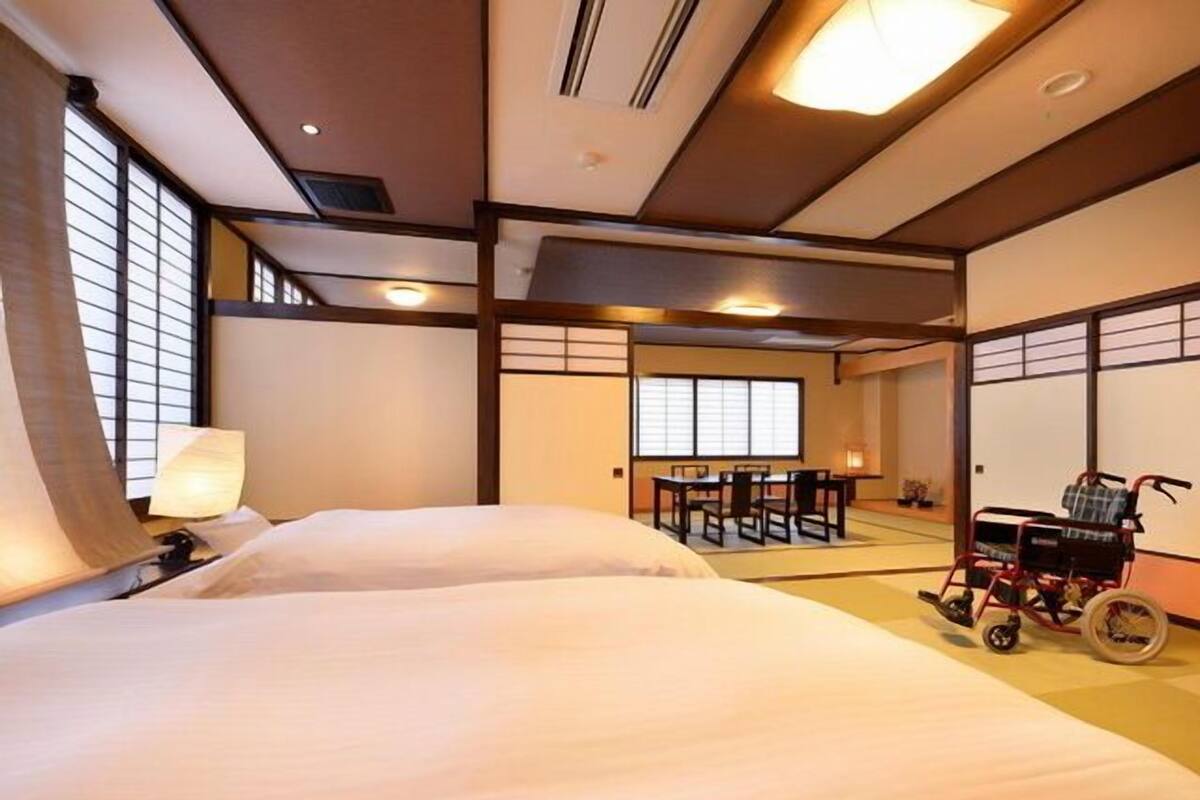 Una habitación tradicional japonesa con suelo de tatami, una mesa baja con sillas y una silla de ruedas.