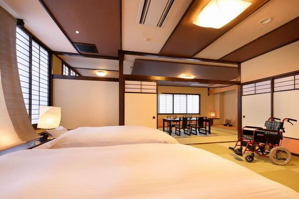 A traditional Japanese-style room with tatami flooring, a low table with chairs, and a wheelchair.