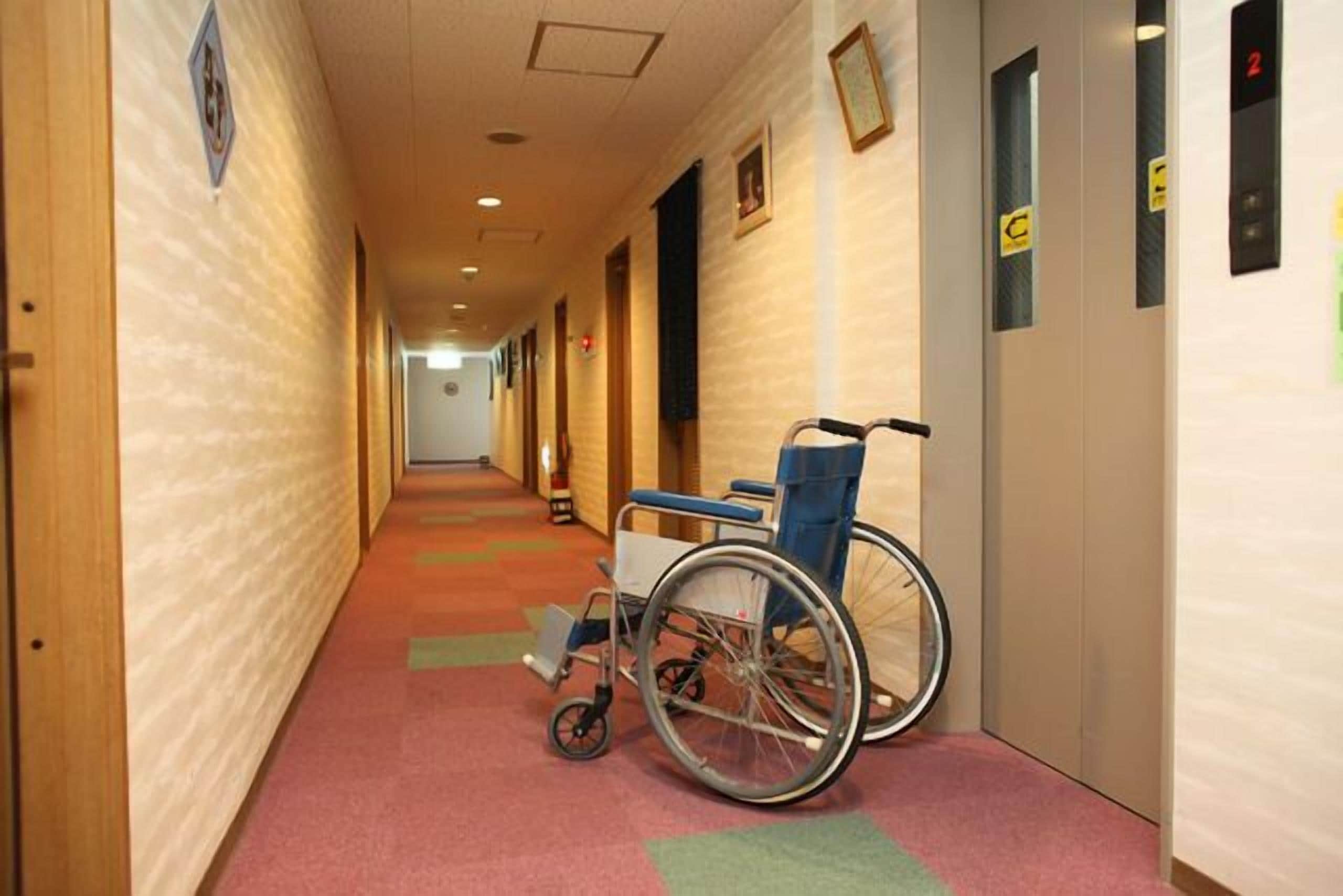 A hotel hallway with a wheelchair, carpeted floors, and doors with numbered signs.