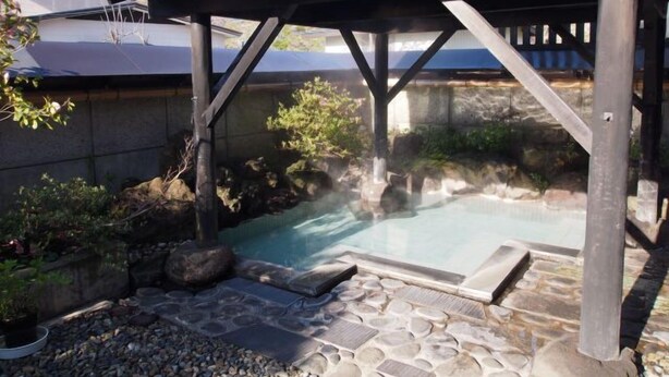 A hot spring area with a stone pathway, wooden deck, and a covered seating area. - Tofuya Ryokan (Yonezawa)