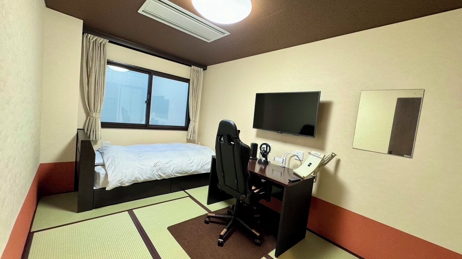 Hotellihuone, jossa on sänky, työpöytä, tuoli, televisio ja ikkuna.