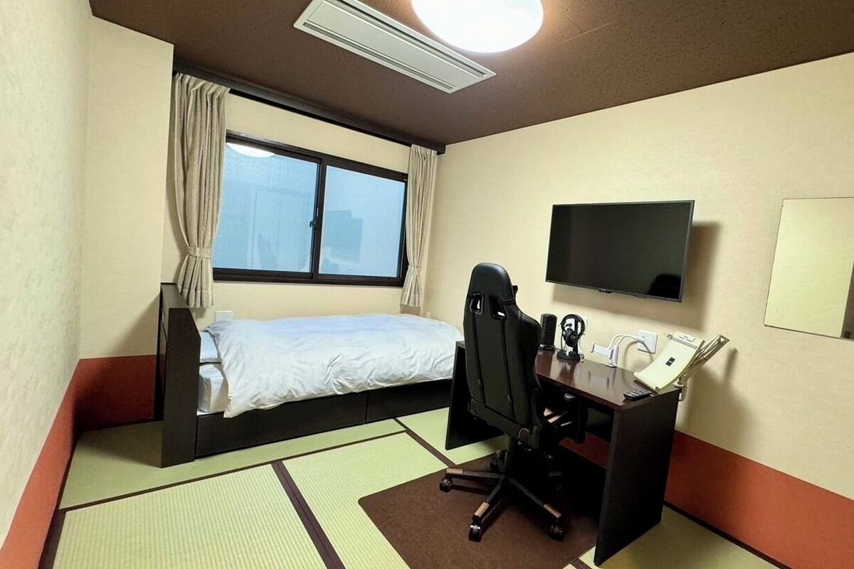 Habitación de hotel con cama, escritorio, silla, televisor y ventana.