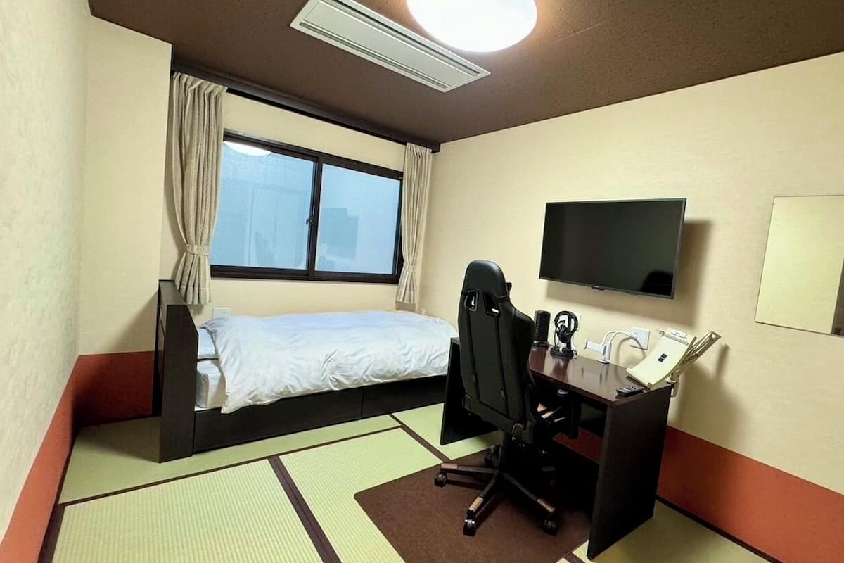 A hotel room with a bed, desk, chair, television, and a window.
