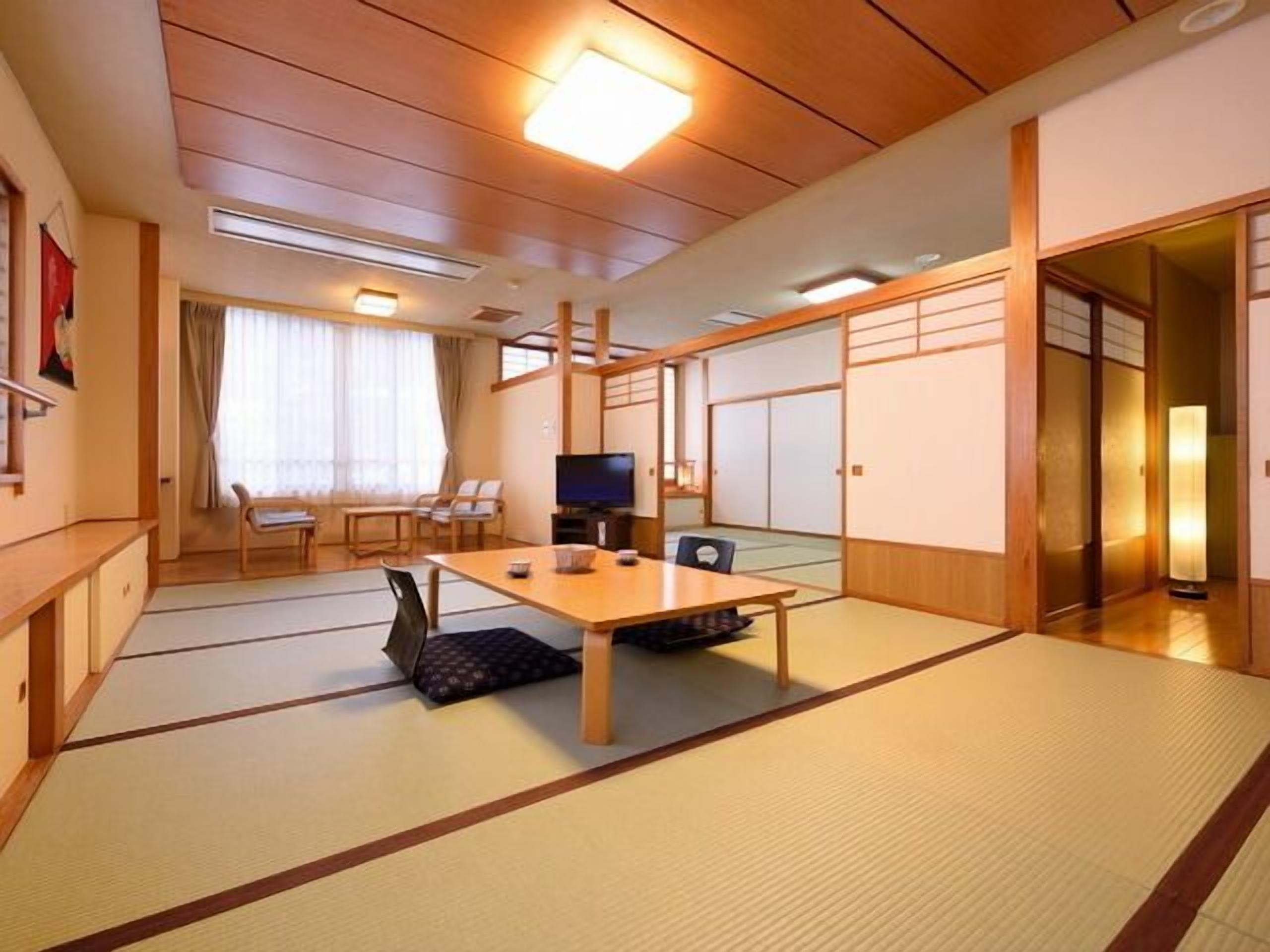 A traditional Japanese-style room with tatami flooring, a low table, chairs, a television, and sliding doors.