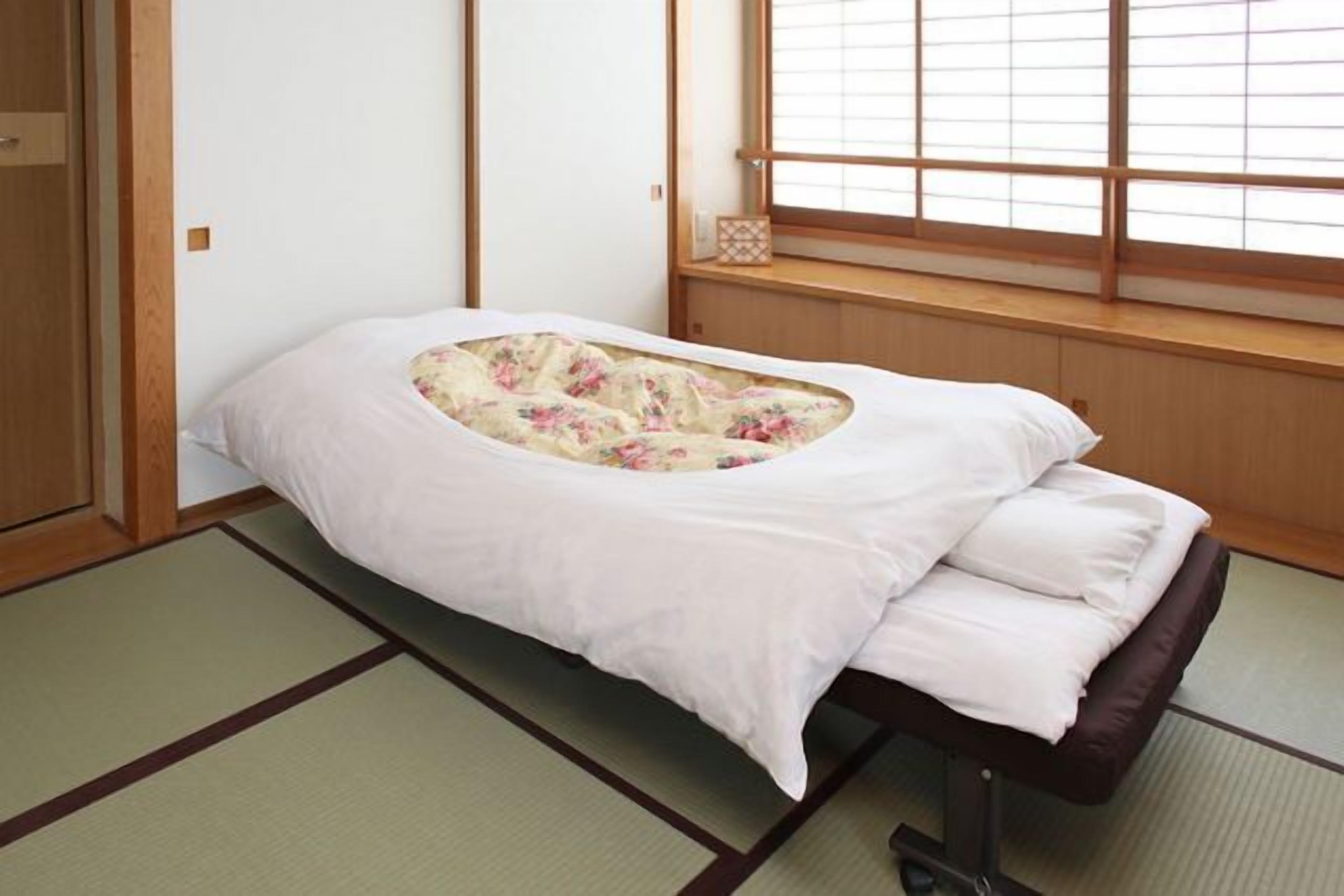 Una habitación japonesa tradicional con suelo de tatami, un futón bajo con estampado floral y una ventana con marcos de madera.