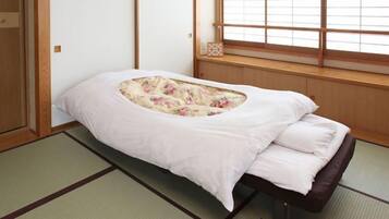 Una habitación japonesa tradicional con suelo de tatami, un futón bajo con estampado floral y una ventana con marcos de madera.