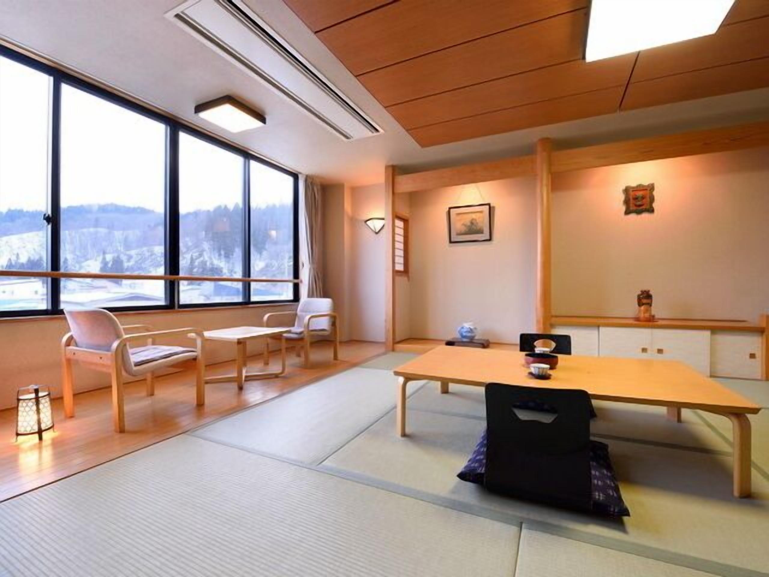 A room with tatami flooring, a low table, chairs, a large window with a view, and a traditional Japanese altar.