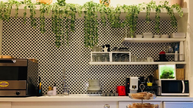 A kitchen with a patterned backsplash, a coffee machine, a microwave, and a glass display case with pastries. - Grande Archivio Napoli 22 (Naples)