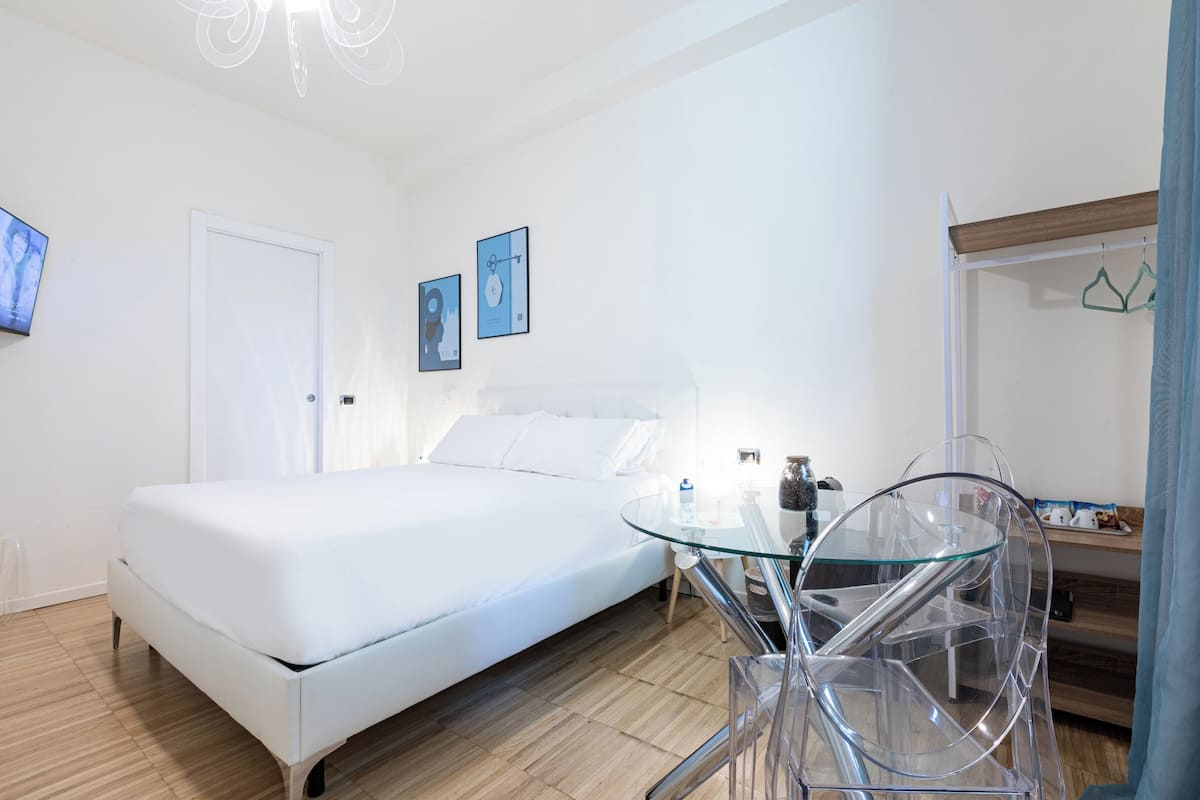 A modern bedroom with a white bed, a glass table, and a wooden floor.