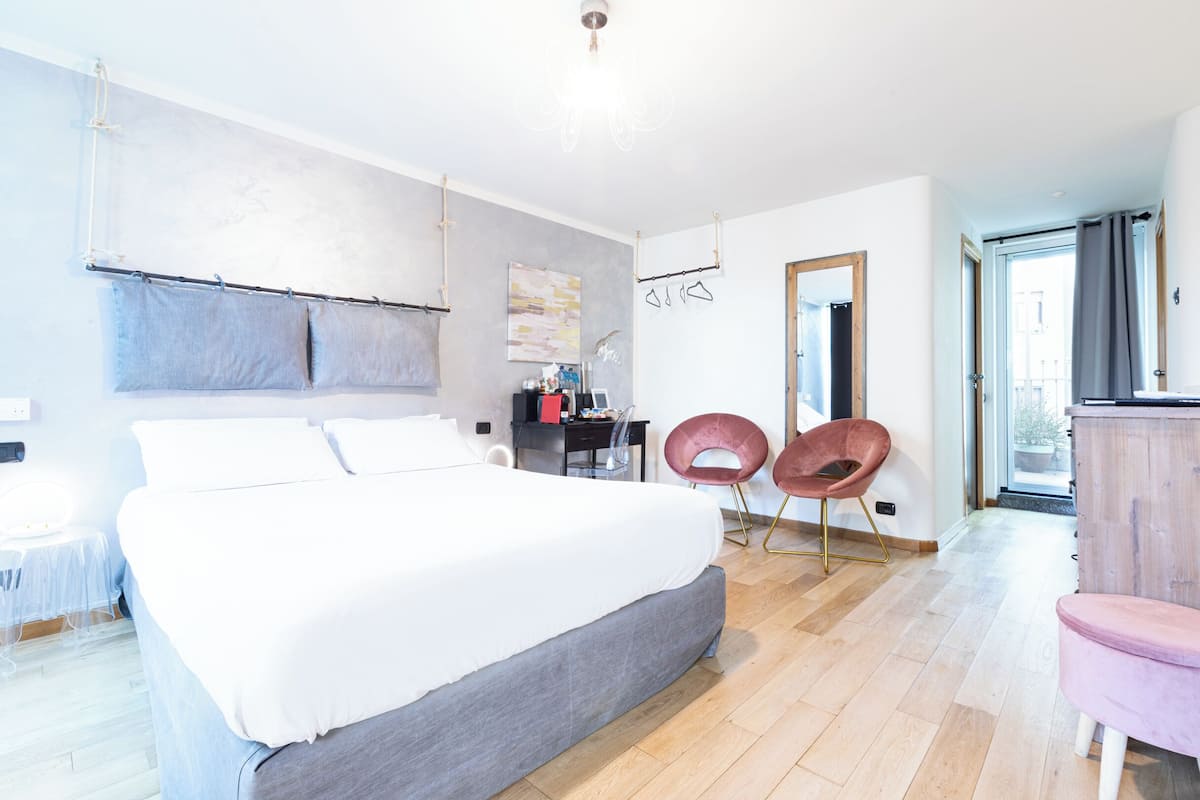 A modern hotel room with a large bed, a desk, two chairs, and a wardrobe.