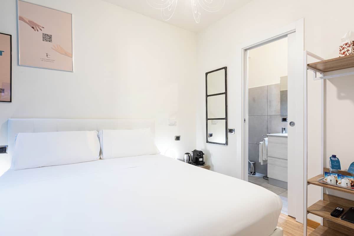 A hotel room with a bed, a bedside table, a mirror, a wardrobe, and a bathroom visible through an open door.
