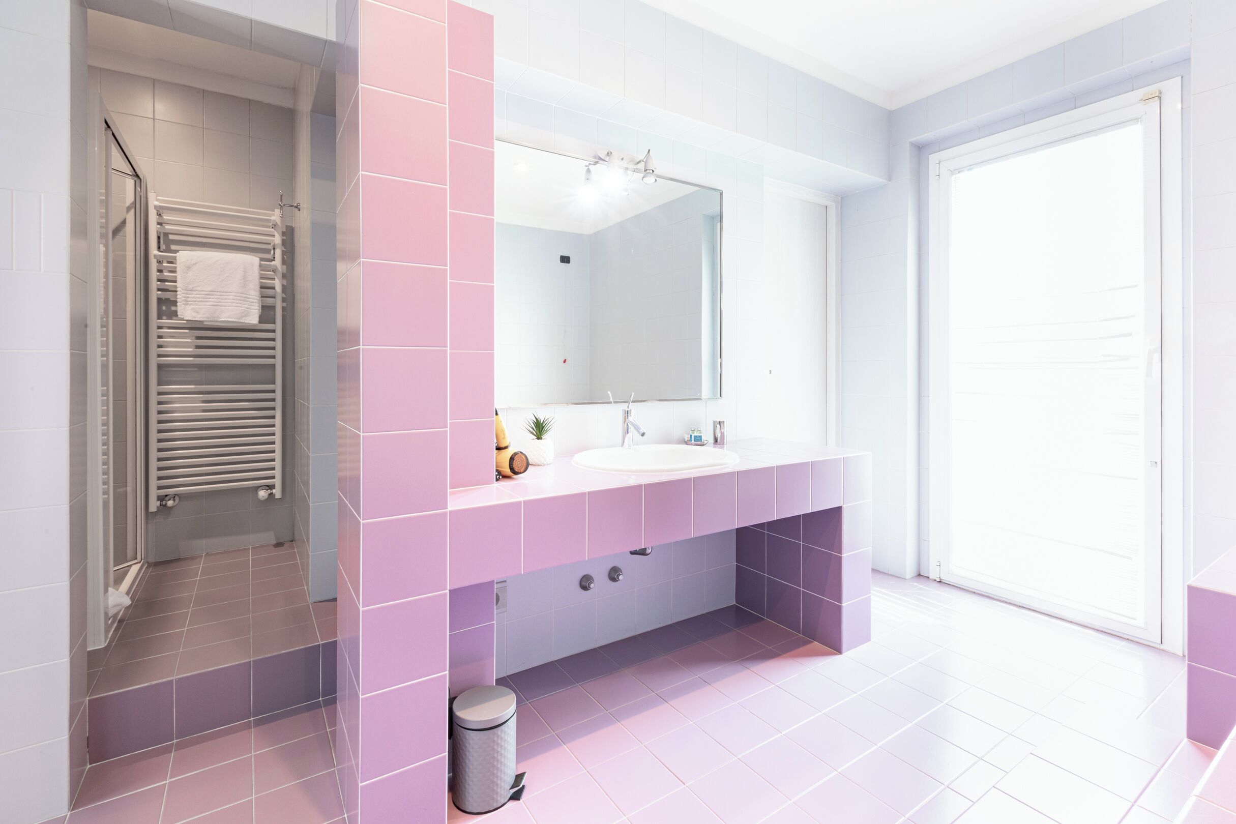 A modern bathroom with a large mirror, white sink, and pink tiles.