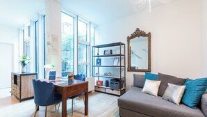 Una sala moderna con una mesa de comedor de madera, sillas azules, un sofá gris con cojines azules y blancos, una estantería y un espejo grande en la pared.