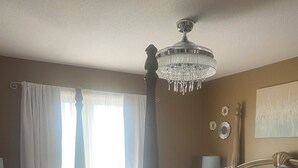 A four-poster bed with a chandelier, a floral bedspread, and a view of the outdoors through sheer curtains.