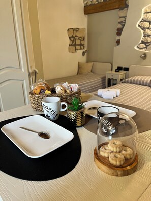 A neatly arranged breakfast table with a coffee mug, a glass of coffee, a plate with a spoon, a basket of pastries, and a small potted plant. - CQ Rooms Verona (Verona)