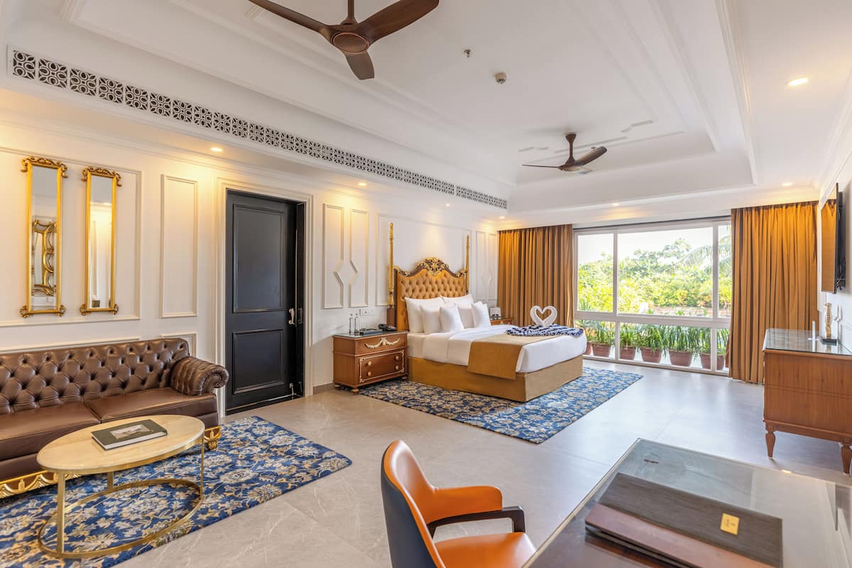 A hotel room with a large bed, a sofa, a coffee table, and a TV.