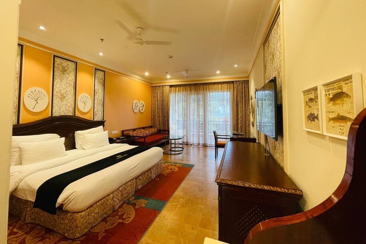 A hotel room with a large bed, a desk, a chair, a TV, and a window with curtains.