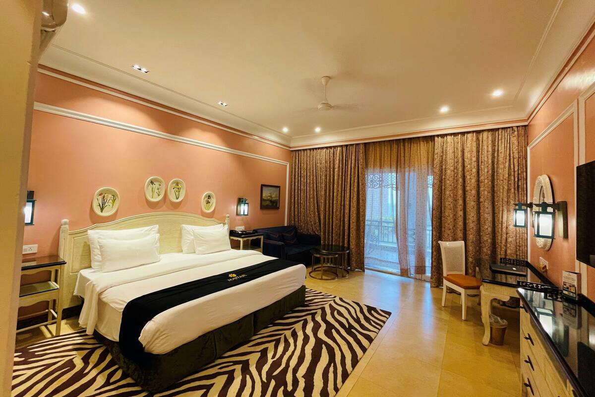 A hotel room with a large bed, a zebra-patterned rug, a desk with a chair, and a television.