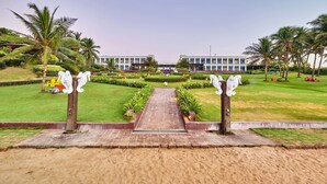 A pathway leading to a building with a symmetrical design, surrounded by well-maintained lawns and palm trees. - Mayfair Palm Beach Resort  (Brahmapur)
